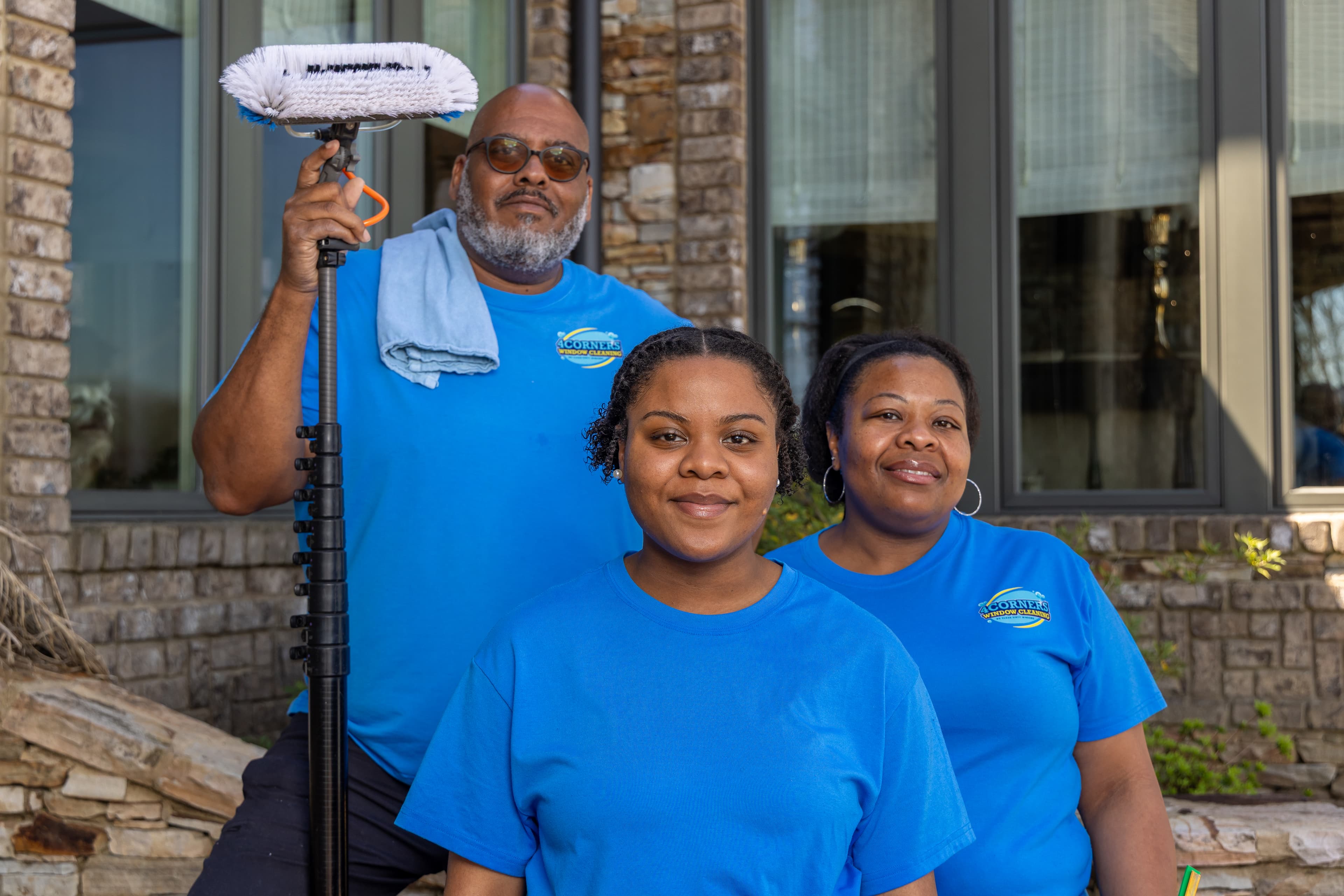 Three window cleaners in blue uniforms posing outside a house with a telescopic brush.